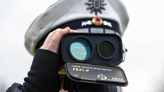 Ein Polizist kontrolliert mit einem Lasermessgerät die Geschwindigkeit der Fahrzeuge.