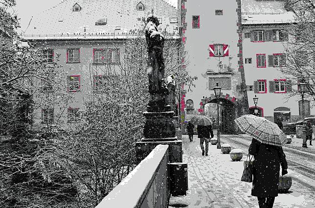 Passanten auf der Seltenbachbrück in Waldshut schützen sich mit Schirmen vor dem Schnee.