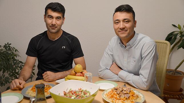 Dilshod Negmatov (links) und Jazur Norkulov mit dem usbekischen Nationalgericht Osch und Gurken-Tomaten-Salat.