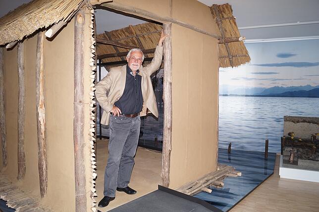 Jörg Heiligmann in einem Nachbau der Pfahlbauten im Museum. Im Hintergrund ein Poster des Bodensee.