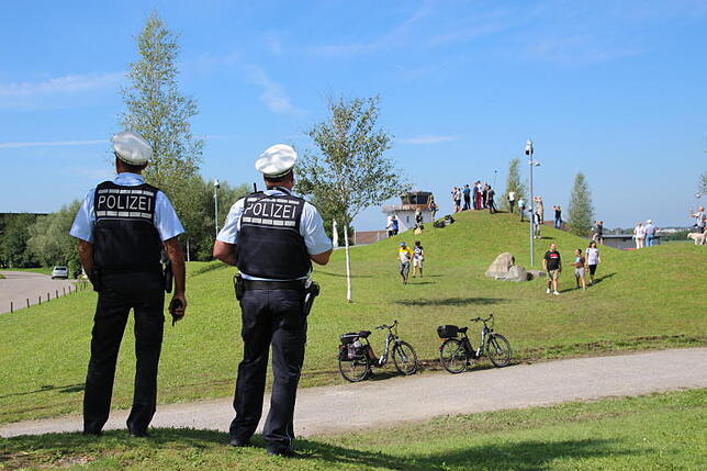 Zwei Polizisten beobachten die Journalisten und Kamera-Teams, die vom Hügel aus Gabriels Ankunft am Dornier-Museum filmen. Dort, wo ...