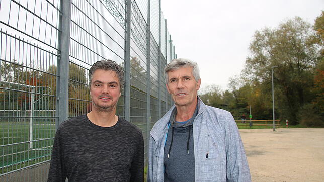 Am Zaun des Kunstrasenplatzes auf der Mettnau stehen Michael Jentsch (links) und Axel Tabertshofer von der IG Sport. Im Hintergrund soll ...