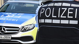 Ein Polizist steht vor dem Dienstwagen (Symbolbild). Nach zwei nächtlichen Angriffen mit einem Pfefferspray und einem Gartenwerkzeug auf ...