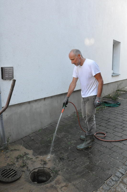 Anwohner Peter Strobel reinigt das Pflaster vor seinem Haus von dem klebrigen Schlamm.