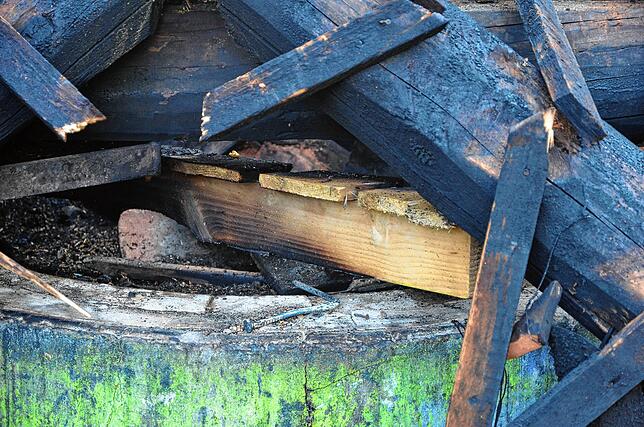 Unter Teilen des angekohlten Balkengerüsts der Grillhütte sind am Montag noch angesengte Paletten zu erkennen. Die Polizei ermittelt in ...