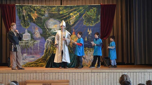 Prinz Tamino (links) erhält von „Den drei Knaben“ unter Anleitung des Priesters Sarastro (Mitte) seine Prüfungsaufgaben. (von links: ...
