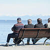 Vier Männer sitzen in Konstanz auf einer Bank am Ufer und blicken auf den Bodensee hinaus. Bild: dpa