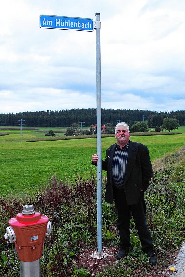 Ortsvorsteher Horst Kritzer mit dem frisch montierten Straßenschild &bdquo;Am Mühlenbach&ldquo; am Neubaugebiet.