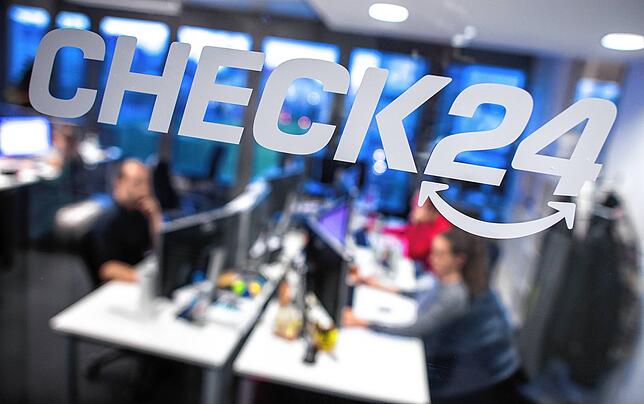 Mitarbeiter sitzen in der Zentrale des Vergleichsportals Check24 in München. Auf der Glasscheibe ist das Logo zu sehen.