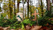 Eine Urne und ein Holzkreuz stehen in einem Friedwald (Symbolbild). Für immer mehr Menschen ist der Wald der beste Platz für die letzte ...