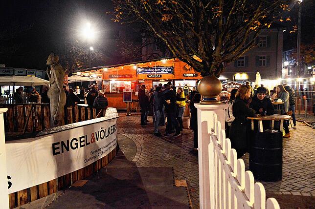 Besucher stehen in kleinen Gruppen an den Stehtischen. Sie trinken Glühwein oder Punsch, essen Pommes oder eine Wurst &ndash; und freuen ...