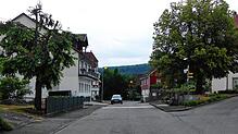 Die Burgfeldenstraße, rechts der Brunnen und die Dorflinde, vorne und hinten die Einmündungsarme der Lindenstraße. Parkende Autos, ...