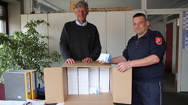 Markus Esterle und Christian Pflumm (von links) mit einer Kiste voller Lolli-Tests. Im Keller des Rathauses stapeln sich nach Wegfall ...