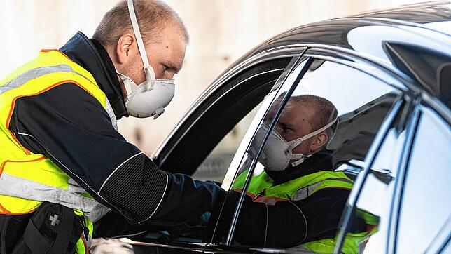 Ein Bundespolizist mit Atemmaske kontrolliert am Grenzübergang zur Schweiz ein Fahrzeug.