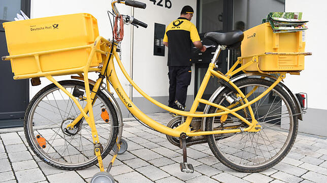 Ein Briefträger der Deutschen Post bei der Zustellung von Briefen mit einem Postfahrrad. Das Logistikunternehmen steht in der Kritik, ...