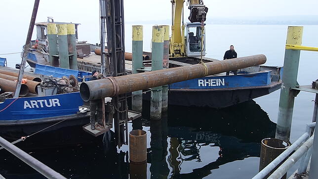 Der erste Teil der neuen Dalbe ragt schon aus dem Wasser. Das zweite Stück bringt der Bagger in die richtige Position, wo es dann ...