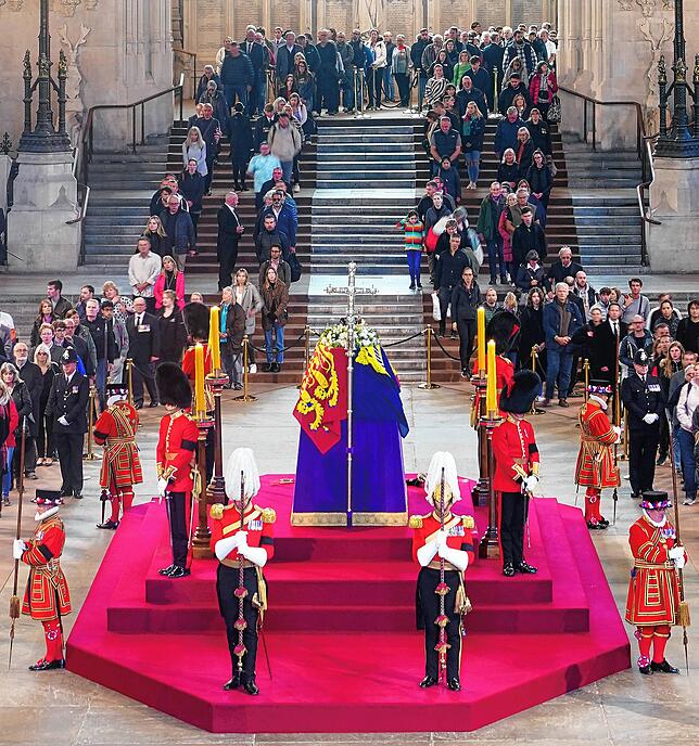 Menschen gehen am Sarg von Königin Elisabeth II. vorbei, der mit der königlichen Standarte, Königskrone, dem Reichsapfel und dem Zepter ...