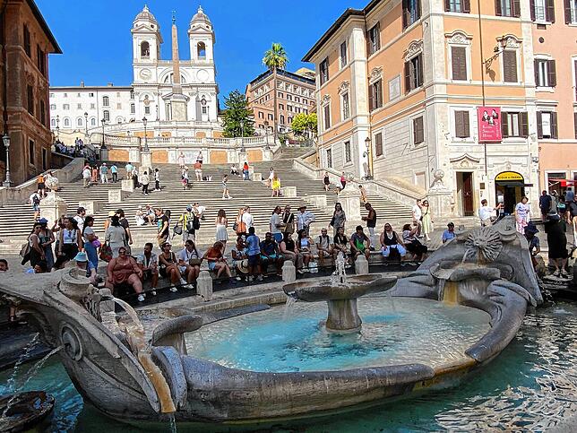 Touristen sitzen im Schatten an der Fontana della Barcaccia vor der Spanischen Treppe in Rom.