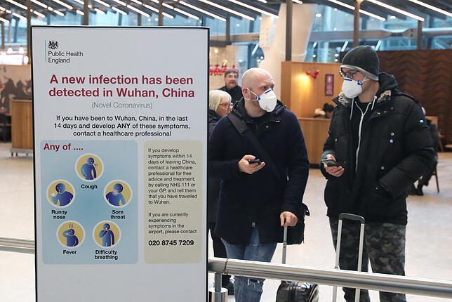 Passagiere mit Mundschutzen am Londoner Flughafen Heathrow . Auf einer Tafel sind Symptome des Coronavirus aufgeführt sowie ...