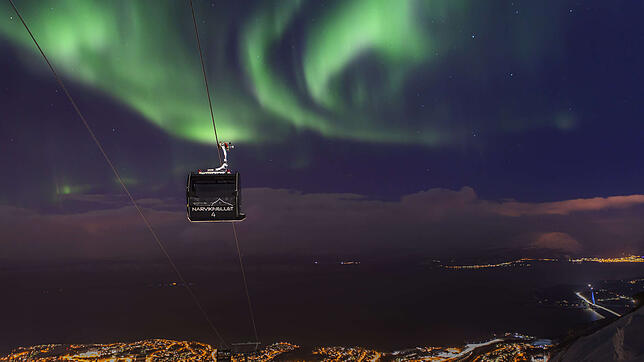 Am Himmel die Polarlichter, unter einem der dunkle Fjord und die Lichter von Narvik: Im Frühherbst und Spätwinter kann man dieses ...
