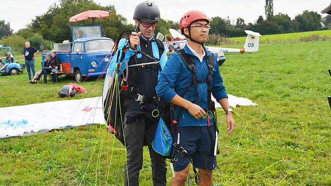 Gleitschirmflieger Nicolas Weber gurtet seinen Tandemmitflieger Jianxiong Zehng fest.