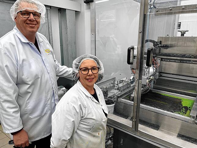 Thorsten Walz und Irina Hupfer stehen an einer Maschine, an der die Aufdrucke für die Tortendekorationen produziert werden.
