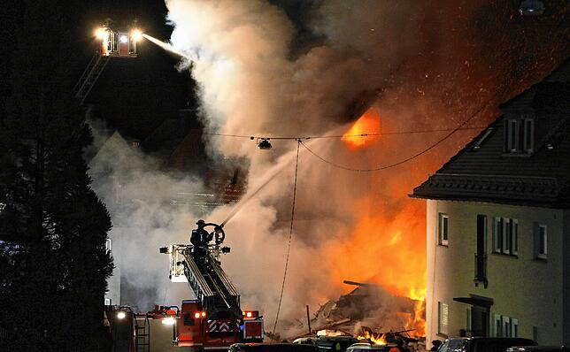 Feuerwehrleute auf Drehleitern löschen in der Nacht das Wohnhaus.