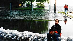 Susanna Katzschke sitzt am Überlinger Mantelhafen auf einer Barriere aus Sandsäcken. Der Bodensee im Hintergrund schwappt über die ...