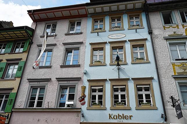 Links rosa, rechts hellblau &ndash; aber einst waren diese beiden Gebäude ein großes Haus. Das Wappen in der Mitte der Fassade zeigt es.