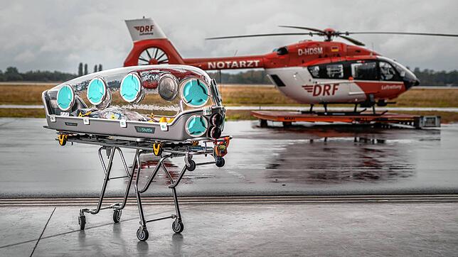 So geht Luftrettung in der Corona-Pandemie: Ein &bdquo;EpiShuttle&ldquo;, eine neuartige Isoliertrage, vor einem DRF-Hubschrauber. Mit ...