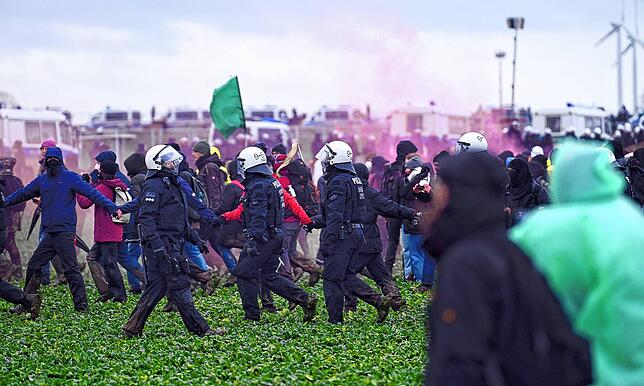 Rauch von Pyrotechnik ist zwischen Polizisten und Demonstranten bei der Demonstration von Klimaaktivisten bei Lützerath unter dem Motto ...