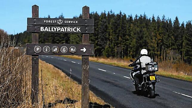 Ein Straßenschild zeigt den Weg in den Wald Ballypatrick Forest, an dem ein Motorradfahrer vorbeifährt. In dem Wald wurde am 20. April ...