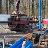 Wasser spritzt aus dem Bohrloch, als Arbeiter der Brunnenbaufirma die Versuchspumpe Rohrsegment für Rohrsegment zurück an die Oberfläche ...