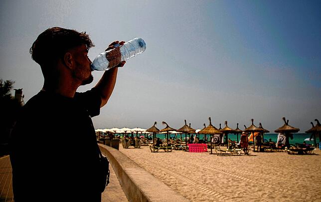 Etienne di Biberach beve acqua sulla spiaggia dell'Arenal a temperature elevate.