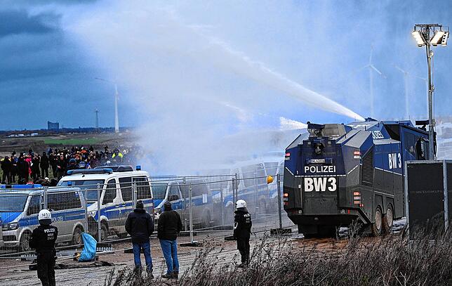 Die Polizei fährt mit einem Wasserwerfer bei einer Demonstration an Klimaaktivisten vorbei.