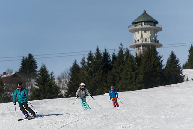 Skifahrer fahren auf dem Feldberg im Schwarzwald die Piste hinab.