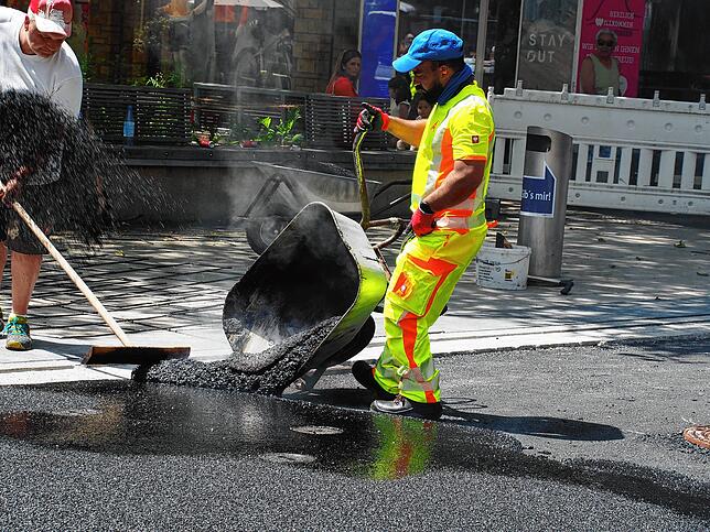 Heißer Job an heißen Tagen: Ein Mitarbeiter der Offenbacher Asphaltfirma kippt den heißen Asphalt auf die Erzbergerstraße.
