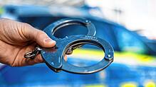 Eine Hand hält Handschellen vor einen Streifenwagen der Polizei (Symbolbild). Seiner Verhaftung entging ein 26-Jähriger in Basel &ndash; ...