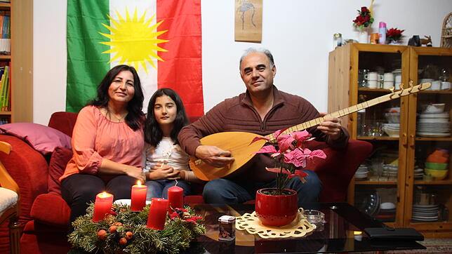Shahnaz Gallo (von links), Shana und Jihad Youssef, mit dem Musikinstrument Tanbour, sitzen vor der kurdischen Flagge. Auf dem Tisch ...