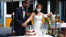 Auch beim Anschneiden der Hochzeitstorte fehlte der für das Brautpaar eigens individuell angefertigte Mundschutz nicht. Im Hintergrund ...