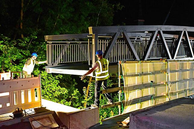 Zwei Arbeiter auf jeder Seite achten darauf, dass die Brücke zentimetergenau in die vorgesehene Fundamentaussparungen passt.