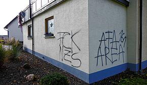 Diese Schmierereien wurden an eine Hauswand gesprüht. Links ist das beschädigte Fenster zu sehen.