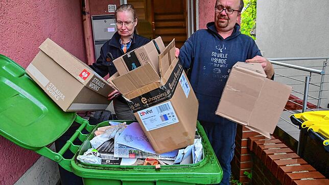 Karen Bossio und Sven Lichey stopfen Kartonagen in die bereits volle Papiertonne. Zur Demonstartion fürs Foto haben sie die Kartons noch ...