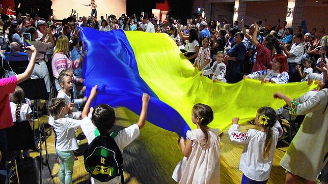 Die Nationalflagge der Ukraine vereint rund 500 Besucher links und rechts der Stuhlreihen beim Schlussakt für den verspätet begangenen ...