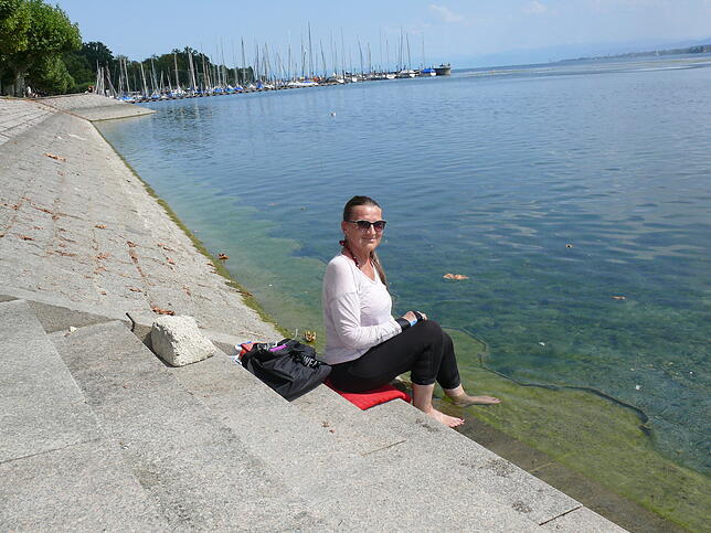 Svetlana Henig sitzt auf einer der untersten Stufen, die an der Seestraße zum See führen. Zu erkennen ist das sehr flache Wasser am Seeufer.