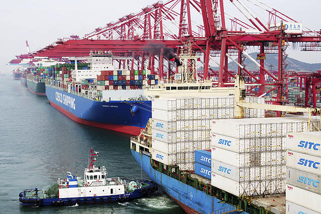 China, Qingdao: Ein Binnenschiff schiebt ein Containerschiff zum Anleger der Werft.