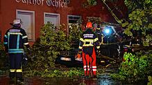 Feurwehrleute arbeiten an einem auf ein Auto gestürzten Baum.