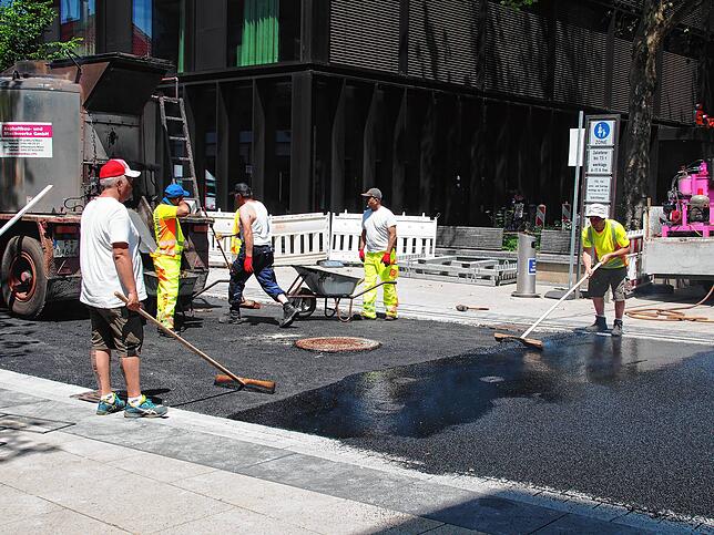 Mit vereinten Kräften wird er heiße Asphalt auf die Erzbergerstraße gekippt und verteilt. Ein hochwertiger Pflasterbelag hatte den ...