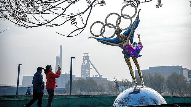 Besucher fotografieren eine Statue von Eiskunstläufern mit den olympischen Ringen in einem Park in der Nähe des Sitzes des Pekinger ...