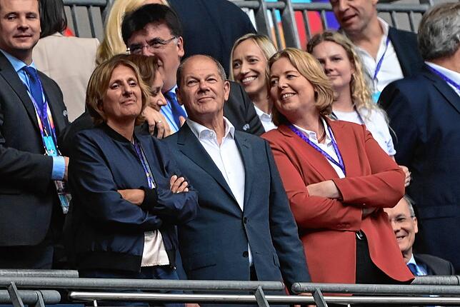 Bundeskanzler Olaf Scholz steht auf der Tribüne mit seiner Frau Britta Ernst (l) und Bundestagspräsidentin Bärbel Bas (r)